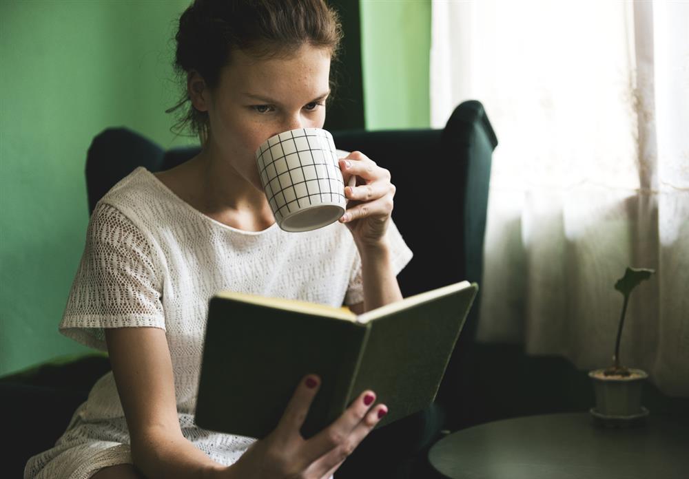 kahve yudumlayarak kitap okuyan kadın